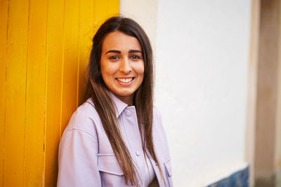 Portrait of a smiling young woman against wall