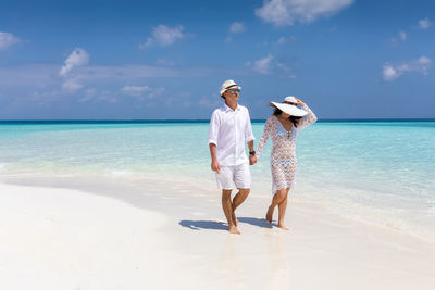 Full length of couple walking at beach against sky