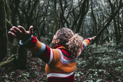 Carefree woman standing with arms outstretched in forest