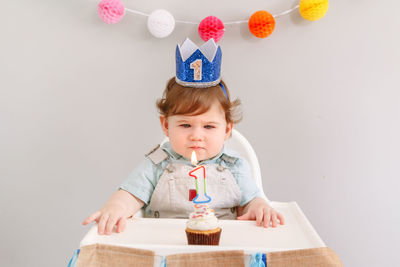 Cute baby boy sitting against wall during birthday