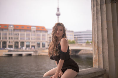 Portrait of woman sitting on window sill against buildings in city