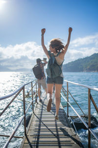 Full length rear view of woman jumping on pier over sea against sky