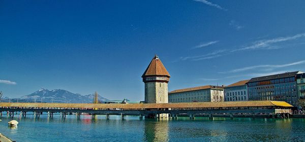 Bridge over river by buildings against blue sky