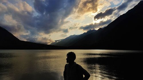Rear view of silhouette man looking at lake against sky