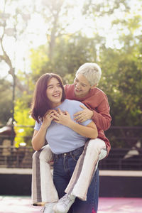 Happy young woman giving piggyback ride to friend on sunny day