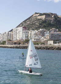 Sailboat in sea by buildings against clear sky