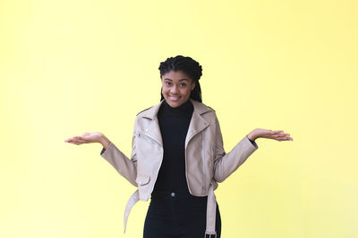Portrait of young woman standing against yellow background
