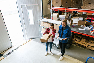 High angle view of male and female coworkers examining cardboard box at distribution warehouse