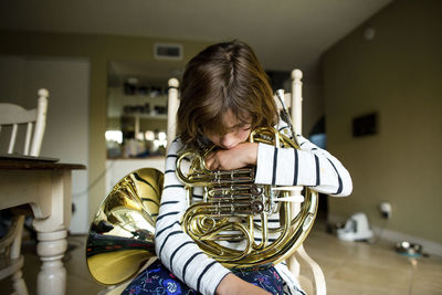Girl with french horn sitting on chair at home