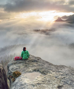 Rear view of man sitting on rock against sky