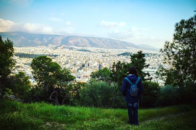 Rear view of man looking at cityscape while standing on grassy hill