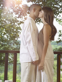 Side view of young couple romancing while standing by railing in balcony