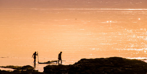 Couple with their canoe by the ocean in front of a sunset