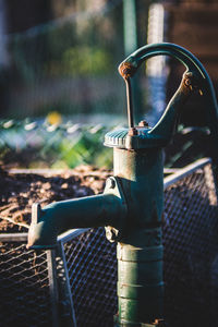 Close-up of faucet on metal fence against blurred background