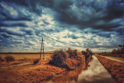 Stream by field against cloudy sky