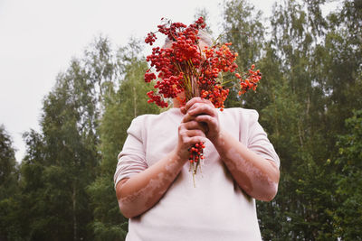 Woman holding red flower against trees