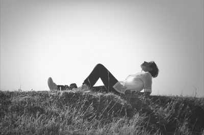 Full length of man resting on grassy field against clear sky