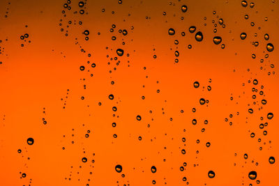 Full frame shot of wet glass against orange background