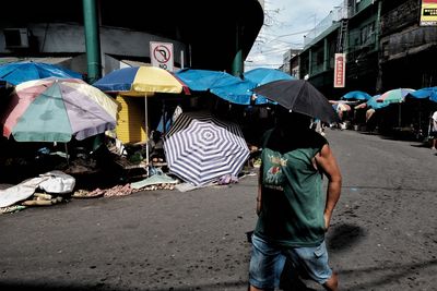 Rear view of man holding umbrella on street during rainy season