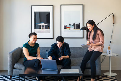 Male and female colleagues discussing over laptop while sitting on sofa at office