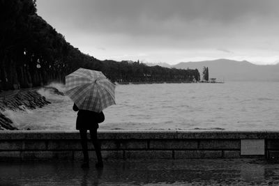 Rear view of woman standing on sea during rainy season