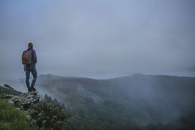 Rear view of man standing on mountain against cloudy sky