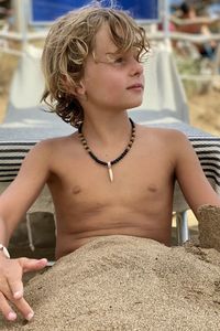 Boy looking away while sitting outdoors in the sand 