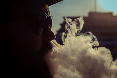 Close-up of man emitting smoke during sunset