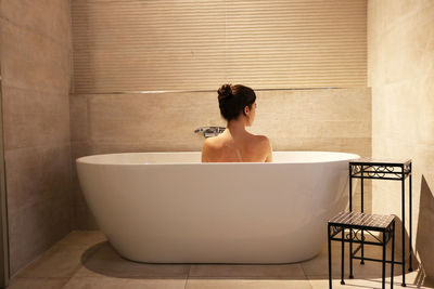 Rear view of shirtless man sitting in bathroom