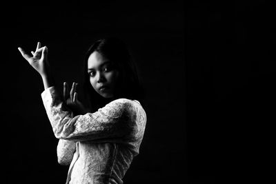 Portrait of woman standing against black background