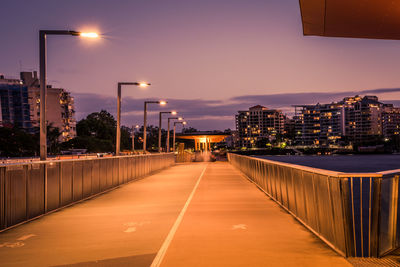 Illuminated street amidst buildings against sky at night