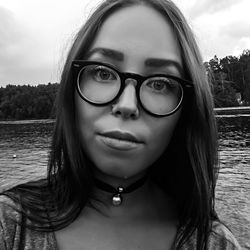 Close-up portrait of young woman wearing eyeglasses against lake