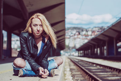 Portrait of young woman sitting at railroad station platform