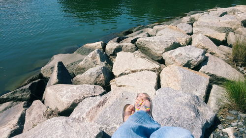 Low section of woman sitting on rock by lake