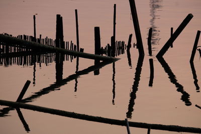 Silhouette wooden posts in lake against sky during sunset