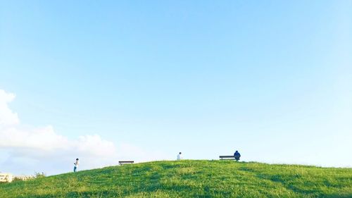 People on grassy field against blue sky