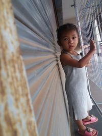 Side view portrait of cute girl standing by closed shutter