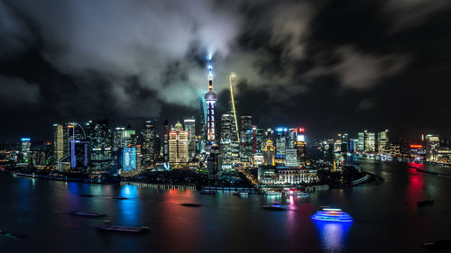 Illuminated buildings by river in city at night