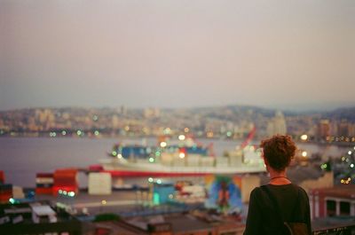 Rear view of man standing in front of river and buildings in city at dusk