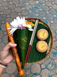 Cropped hand of person holding religious offerings in plate on footpath