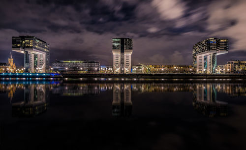 Illuminated kranhaus by river against cloudy sky at night