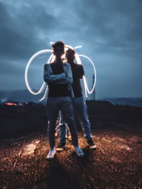 Front view of two people standing against the backdrop of sky and light painting