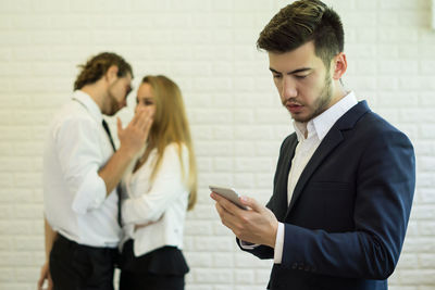 Businessman using phone while standing with colleagues in office