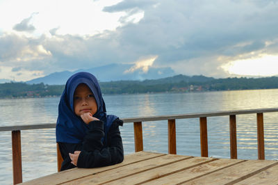 Portrait of boy sitting on wood against sky