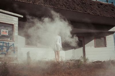 Woman standing amidst smoke by house