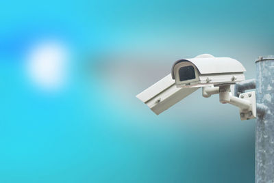 Low angle view of security camera against blue background