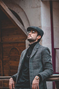 Young man looking away while standing against wall