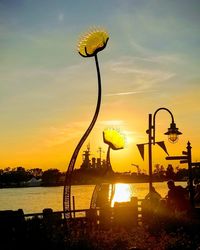 Silhouette plants by lake against sky during sunset