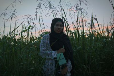 Portrait of young woman standing on field against sky