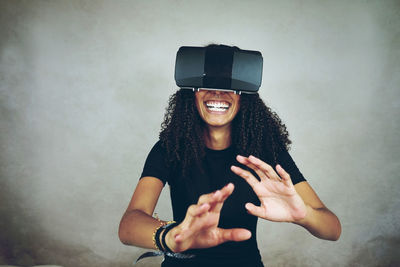 Smiling woman wearing virtual reality simulator while gesturing against wall